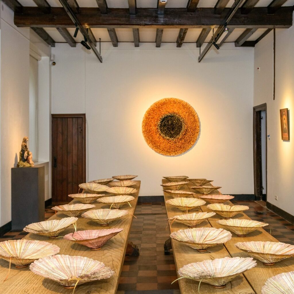 missie blikt uit deze zaal met dakbalken, een oude kloostertafel en ronde, papieren veelkleurige kunstwerken op tafel en aan de muur