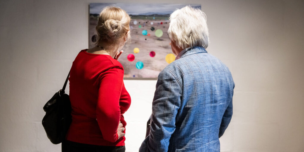 Man en vrouw op de rug gezien terwijl zij een foto bekijken in de tentoonstelling EXODUS